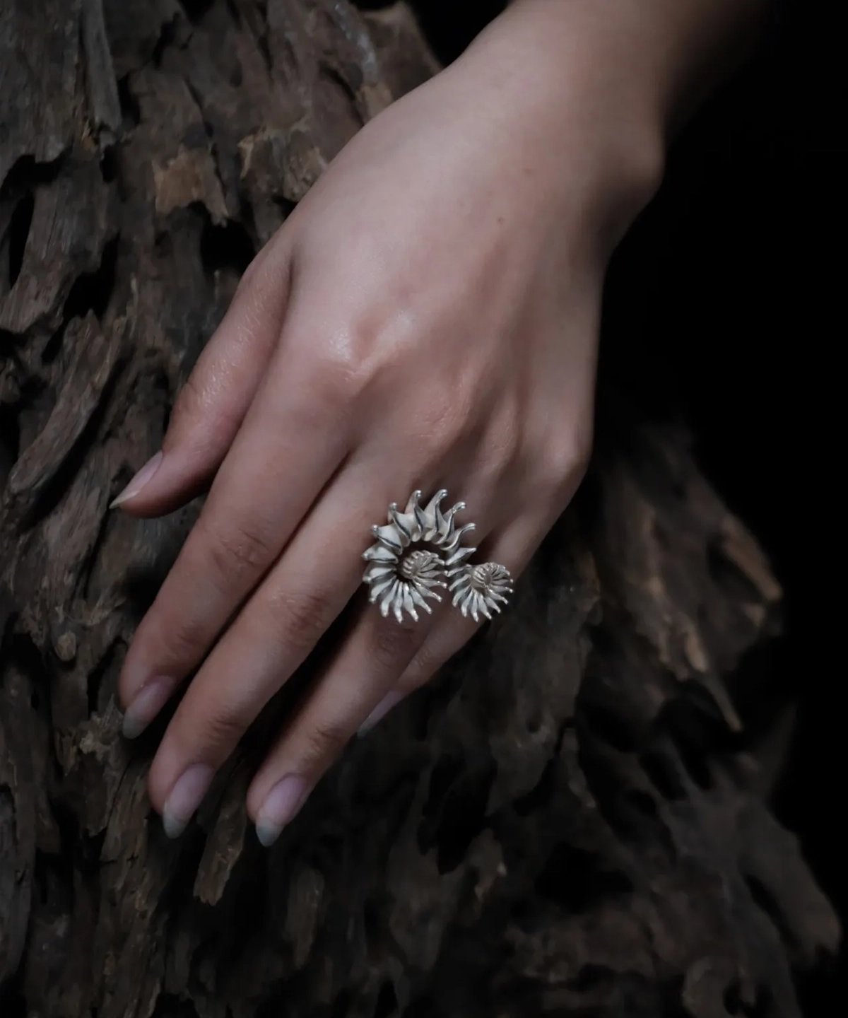 A close-up shot of a hand adorned with a Spiral Ring crafted from S925 sterling silver. The ring features an intertwined, sculptural design, elegantly wrapping around the finger. The hand is placed against a textured wooden backdrop, complementing the organic aesthetic of the jewelry.