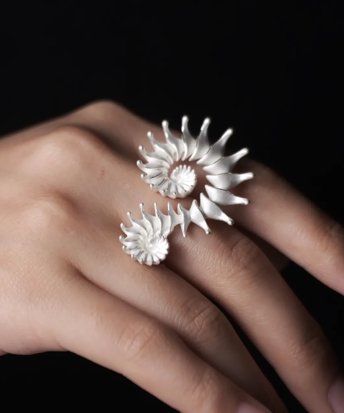 A close-up of a hand adorned with a Spiral Ring, crafted in S925 sterling silver, showcasing its sculptural and artistic design. The fluid, intertwined curves wrap elegantly around two fingers, creating a bold yet sophisticated statement.