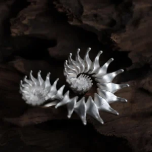 A handcrafted Spiral Ring made of S925 sterling silver, featuring three intricate spiral flower-like structures with delicately curved petals. The sculptural design highlights organic fluidity and artistic craftsmanship. Set against a textured wooden background, the ring's polished finish and dimensional form showcase elegance and sophistication, embodying the essence of a statement Design Ring.