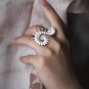 A close-up image of a hand adorned with the Spiral Ring, crafted from S925 sterling silver. The ring showcases an intricate sculptural design with elegant spiral patterns. The hand delicately holds a textured fabric, enhancing the ring’s artistic appeal.