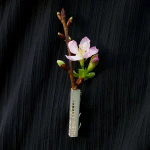 A handmade 925 sterling silver brooch with a delicate branch and pink flower buds, elegantly pinned on black fabric.