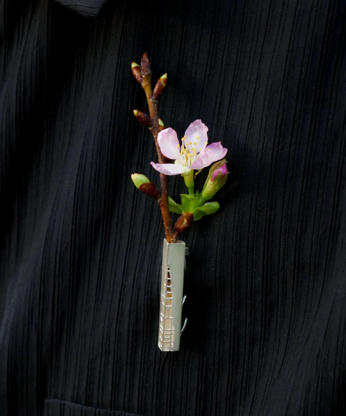A handmade 925 sterling silver brooch with a delicate branch and pink flower buds, elegantly pinned on black fabric.