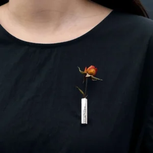 A handmade 925 sterling silver brooch featuring a rectangular silver piece with intricate engravings, elegantly adorned with a dried red rose, pinned on a black shirt.