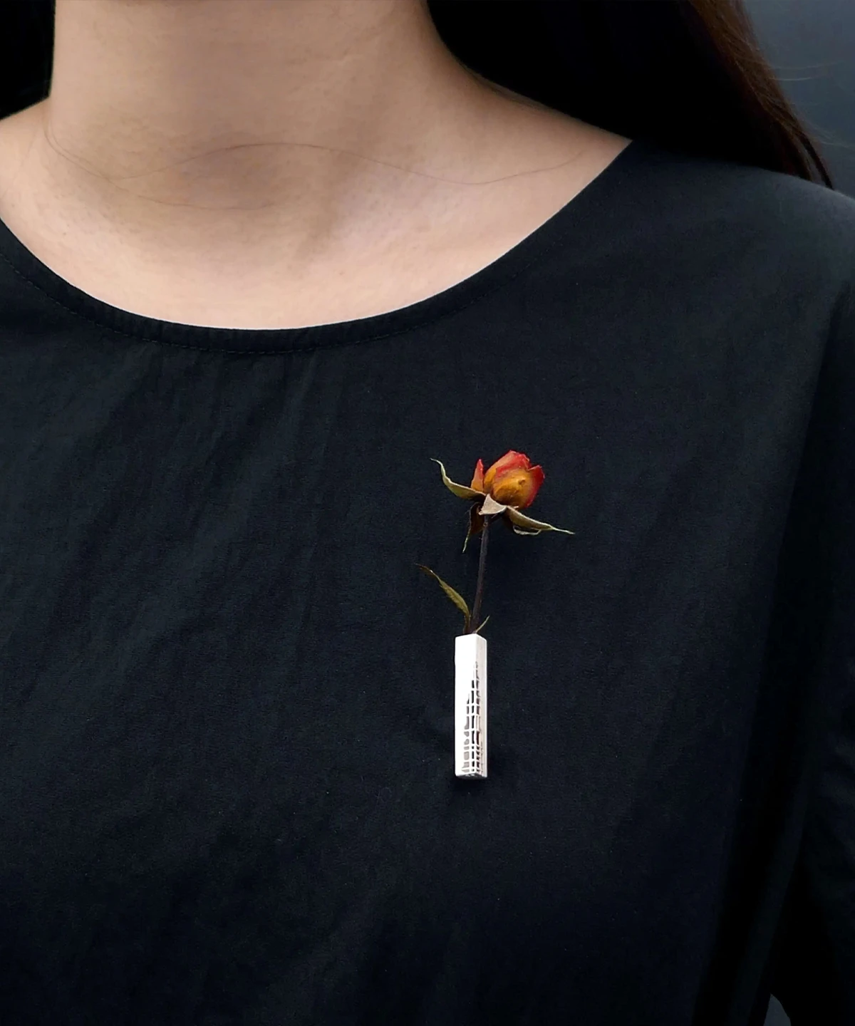 A handmade 925 sterling silver brooch featuring a rectangular silver piece with intricate engravings, elegantly adorned with a dried red rose, pinned on a black shirt.
