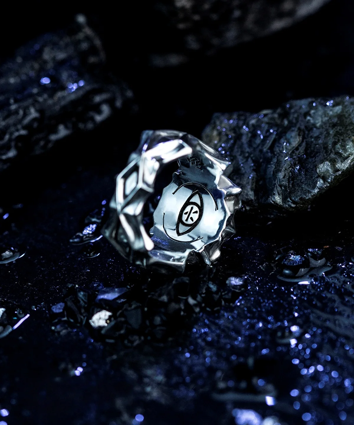 A close-up image of the Vongola Ring Of Hell, handmade in sterling silver with blue spinel. The ring features intricate designs, including an inner band with six engraved characters. The dark, textured background enhances the ring's mysterious and elegant appearance.