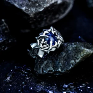 A close-up image of the Vongola Ring Of Hell, a handmade sterling silver ring featuring a natural blue spinel gemstone. Inspired by Mukuro Rokudo from Katekyo Hitman Reborn, the ring showcases intricate details and craftsmanship against a dark, rocky background.