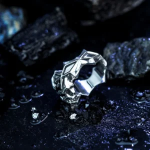 A detailed close-up of the Vongola Ring Of Hell, handmade in S925 sterling silver with a stunning natural blue spinel. The intricate geometric engravings and polished finish reflect its anime-inspired design, set against a moody, textured backdrop.