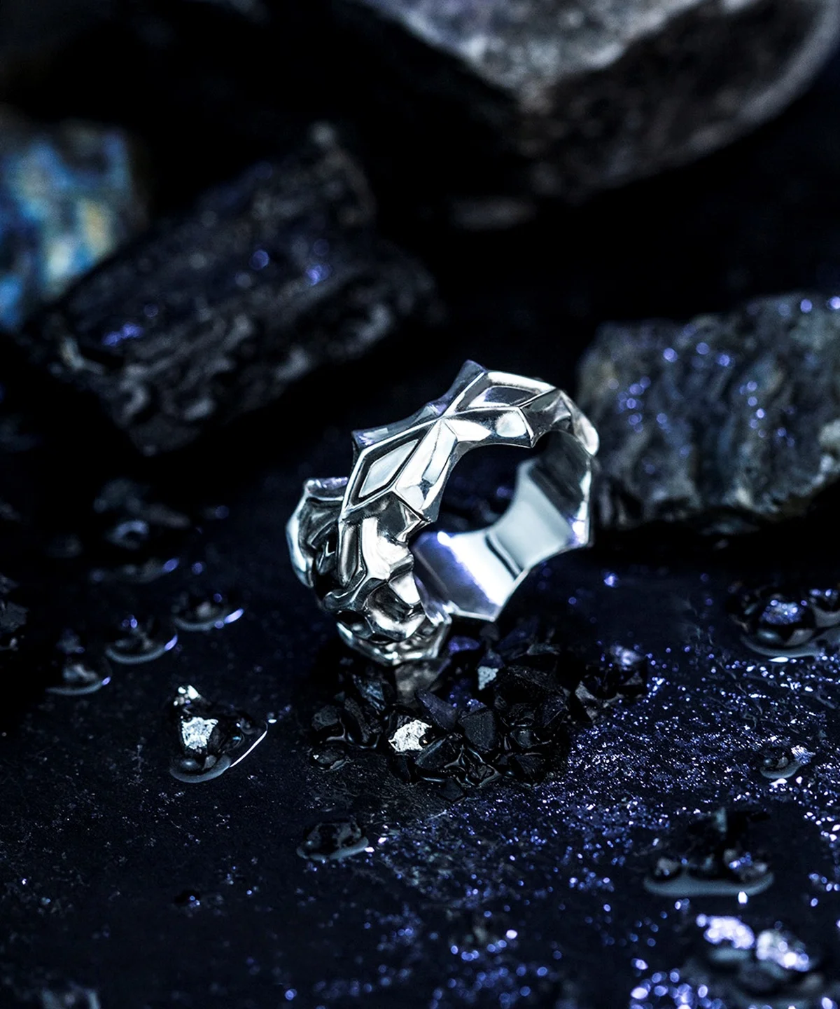 A detailed close-up of the Vongola Ring Of Hell, handmade in S925 sterling silver with a stunning natural blue spinel. The intricate geometric engravings and polished finish reflect its anime-inspired design, set against a moody, textured backdrop.
