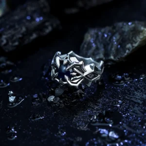 A close-up of the Vongola Ring Of Hell, a handcrafted S925 sterling silver ring featuring intricate detailing and a natural blue spinel gemstone. Inspired by Mukuro Rokudo from Katekyo Hitman Reborn, this anime jewelry piece is displayed on a dark, textured surface with scattered reflective elements, enhancing its allure.
