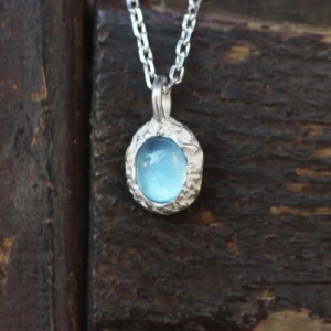 Close-up of a handmade Natural Aquamarine Necklace featuring a light blue aquamarine gemstone in a textured 925 sterling silver pendant. The Lazesoul jewelry rests on rustic wood, highlighting its artisanal charm and elegance.
