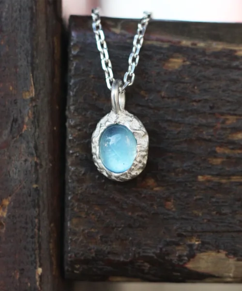 Close-up of a handmade Natural Aquamarine Necklace featuring a light blue aquamarine gemstone in a textured 925 sterling silver pendant. The Lazesoul jewelry rests on rustic wood, highlighting its artisanal charm and elegance.