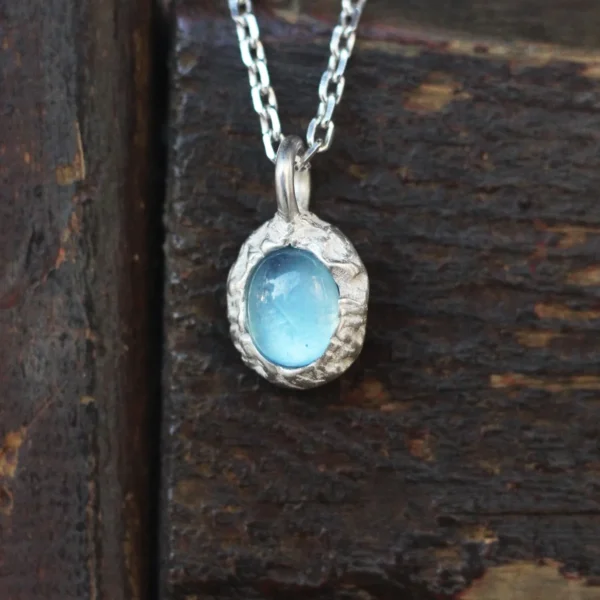925 Silver Natural Aquamarine Necklace 01 Close-up of a handmade Natural Aquamarine Necklace featuring a light blue aquamarine gemstone in a textured 925 sterling silver pendant. The Lazesoul jewelry rests on rustic wood, highlighting its artisanal charm and elegance.