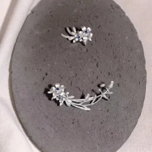 Handmade Lily Earrings in S925 sterling silver with lab-created sapphires; delicate ear cuff design inspired by natural florals, displayed on a gray textured background to highlight craftsmanship.