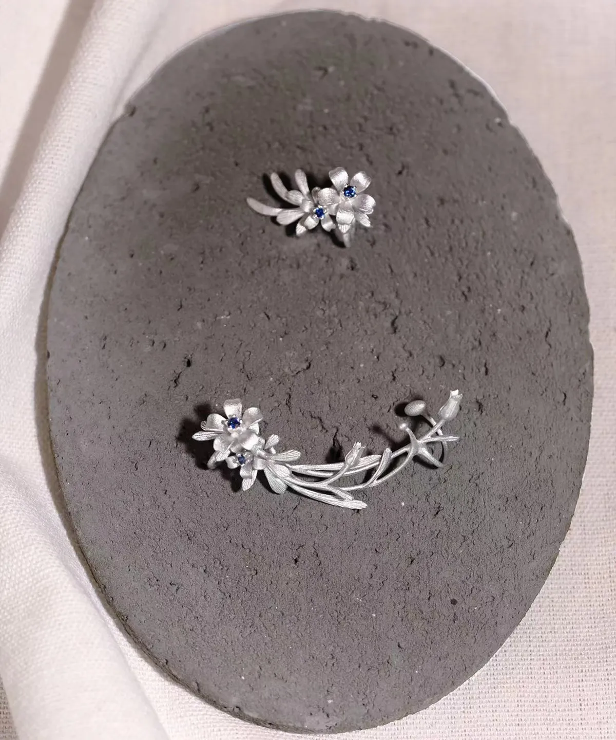 Handmade Lily Earrings in S925 sterling silver with lab-created sapphires; delicate ear cuff design inspired by natural florals, displayed on a gray textured background to highlight craftsmanship.