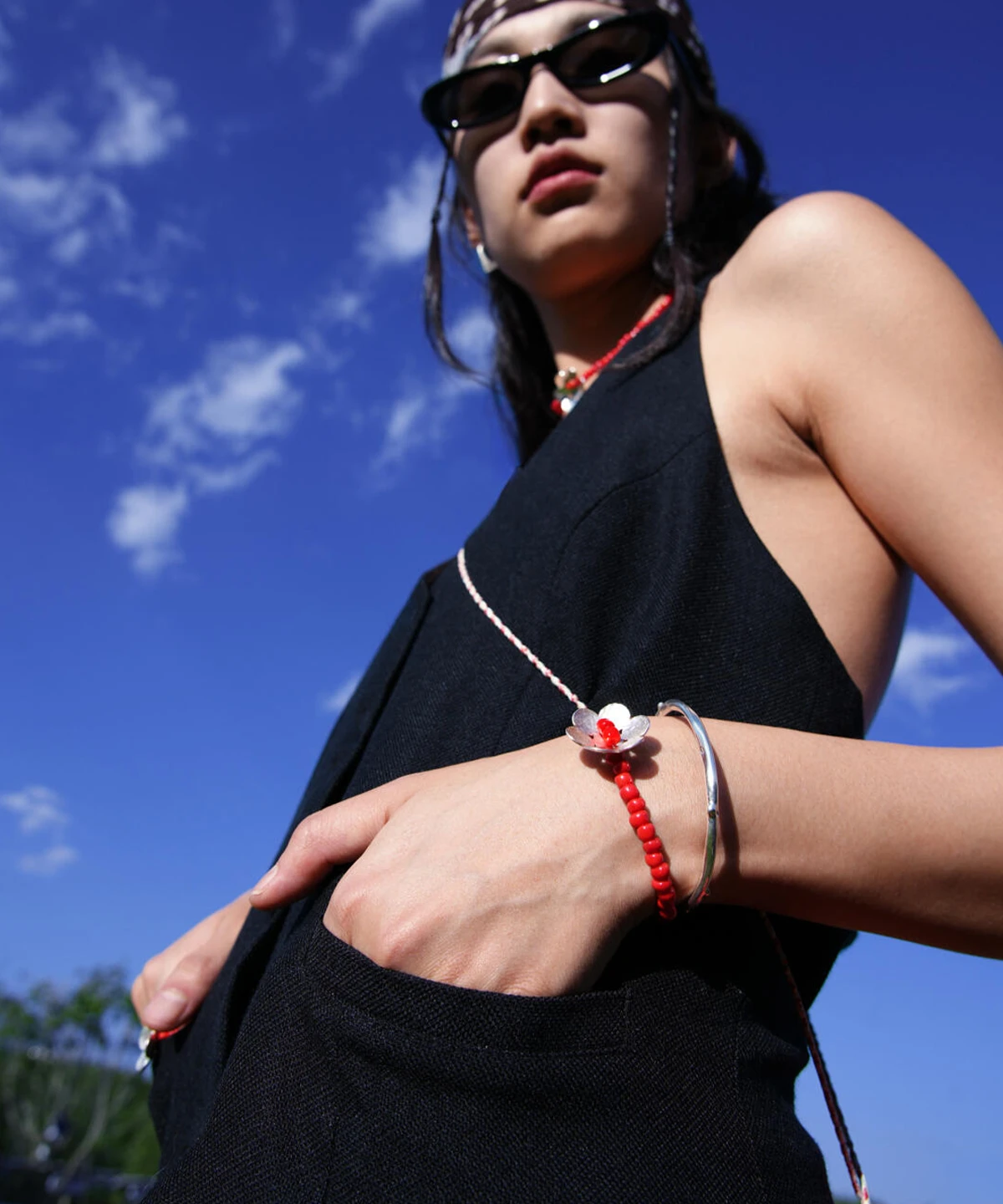 Handmade beaded ring bracelet featuring a sterling silver flower charm and red glaze beads, worn with a black outfit against a blue sky; Lazesoul's S925 sterling silver jewelry.