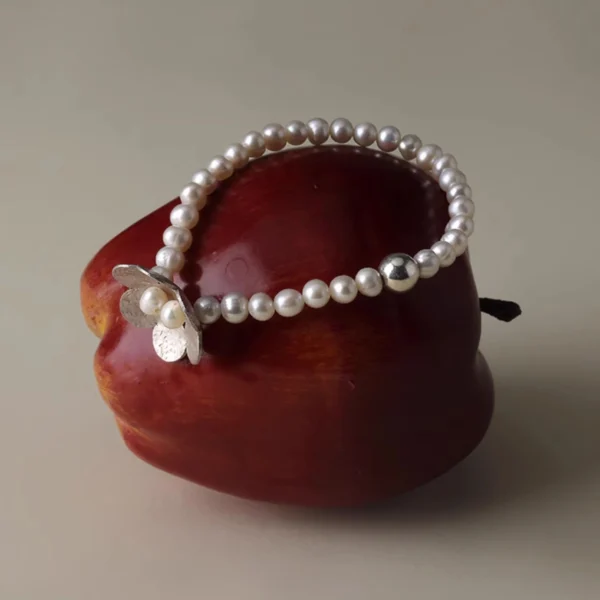 S925 sterling silver beaded ring bracelet with natural freshwater pearl and little flower charm, elegantly displayed on a vibrant red apple for a whimsical, nature-inspired presentation.