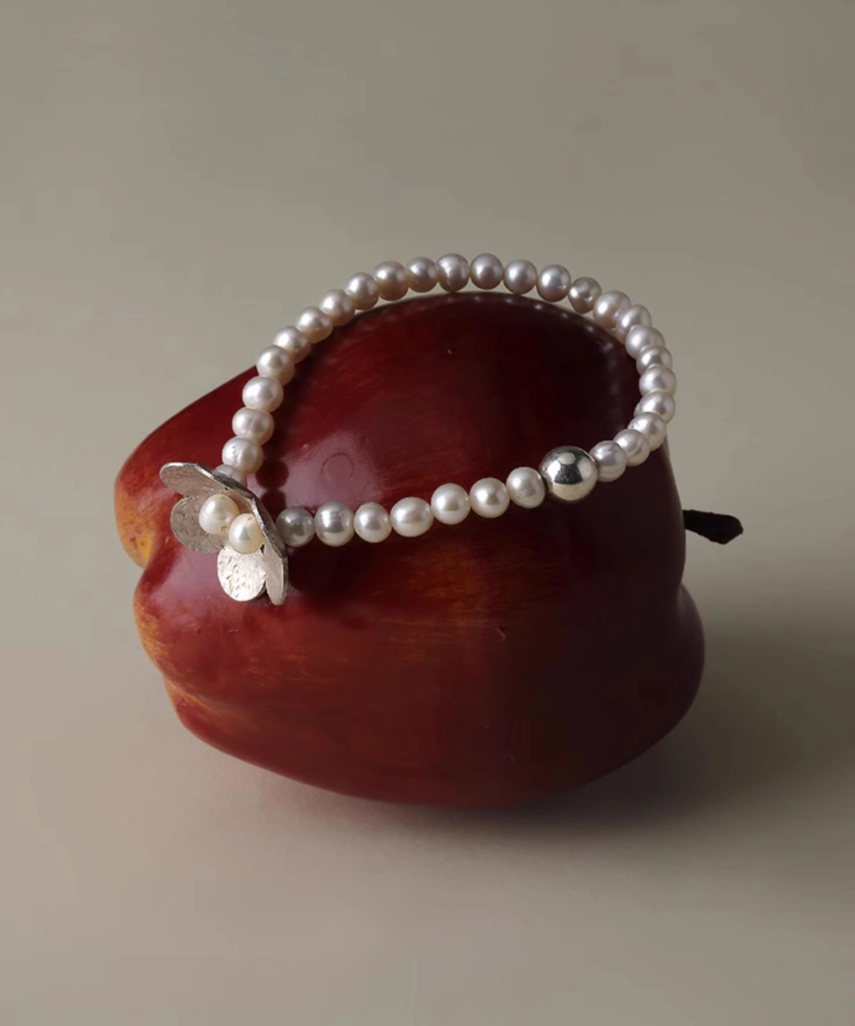 S925 sterling silver beaded ring bracelet with natural freshwater pearl and little flower charm, elegantly displayed on a vibrant red apple for a whimsical, nature-inspired presentation.