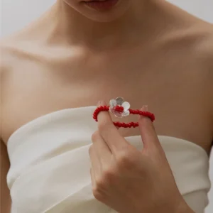 Close-up of a woman wearing a white strapless top, holding a Lazesoul handmade beaded bracelet featuring red glaze beads and a S925 sterling silver flower charm; elegant beaded ring-style jewelry.