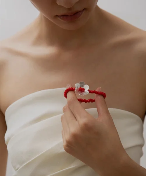 Close-up of a woman wearing a white strapless top, holding a Lazesoul handmade beaded bracelet featuring red glaze beads and a S925 sterling silver flower charm; elegant beaded ring-style jewelry.