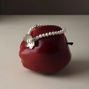 Handmade S925 sterling silver bracelet with little flower charm and natural freshwater pearls, styled on a red apple. Delicate craftsmanship highlights this beaded ring design for natural jewelry lovers.