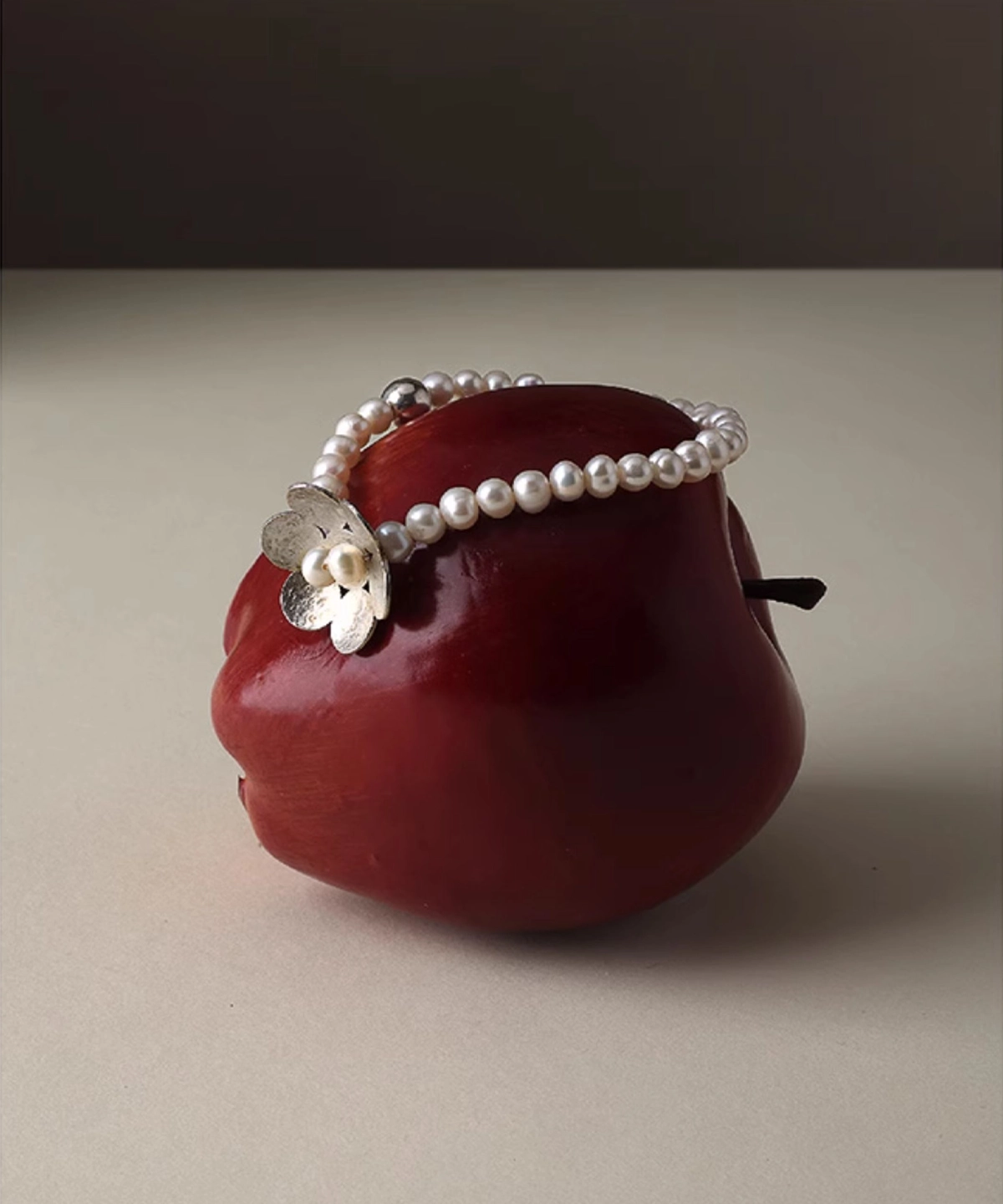 Handmade S925 sterling silver bracelet with little flower charm and natural freshwater pearls, styled on a red apple. Delicate craftsmanship highlights this beaded ring design for natural jewelry lovers.