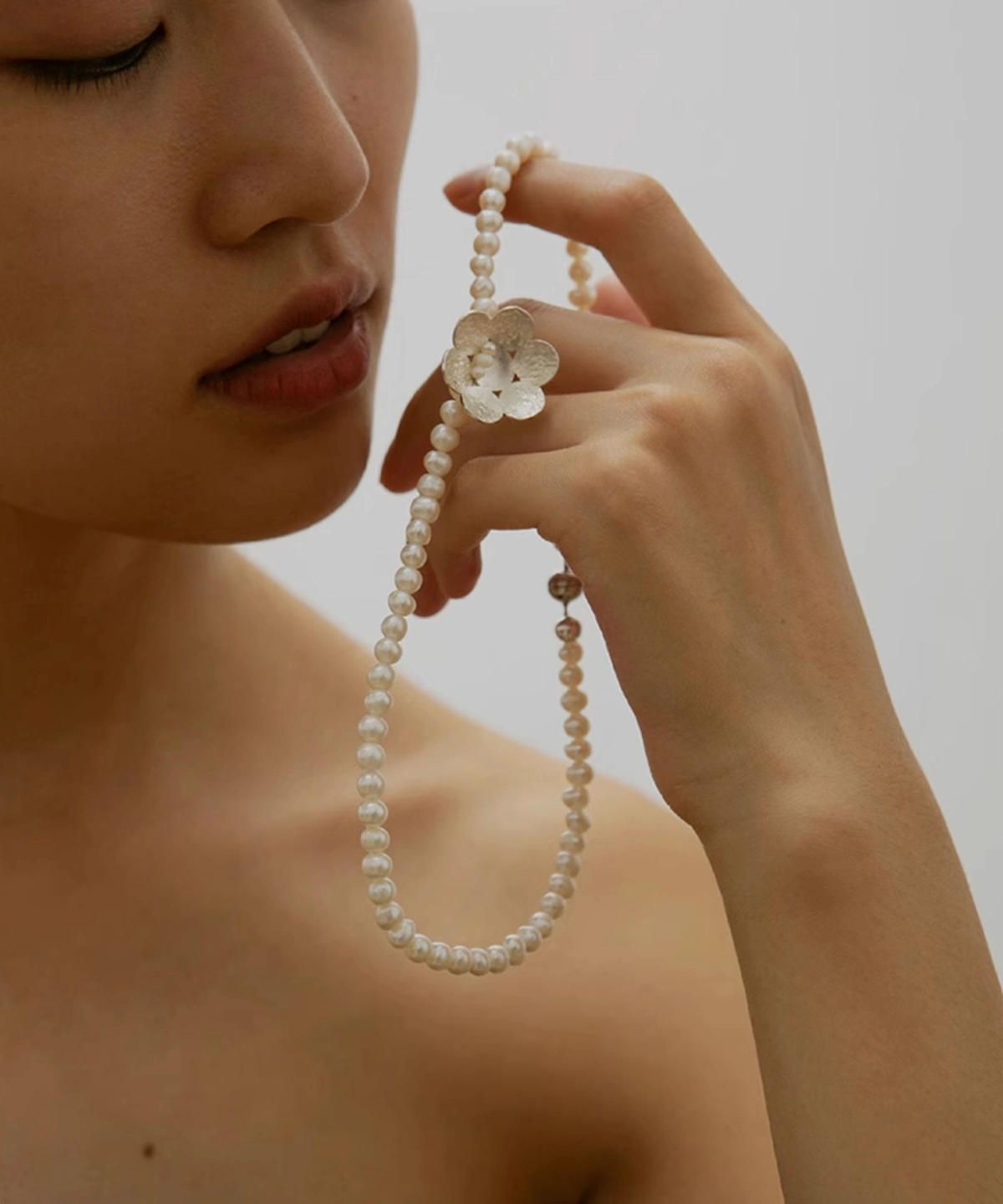 Hand holding Lazesoul Handmade S925 Sterling Silver Little Flower Beaded Necklace with natural freshwater pearl beads and an intricately detailed silver flower charm. The elegant beaded necklace drapes gracefully against a soft neutral background.