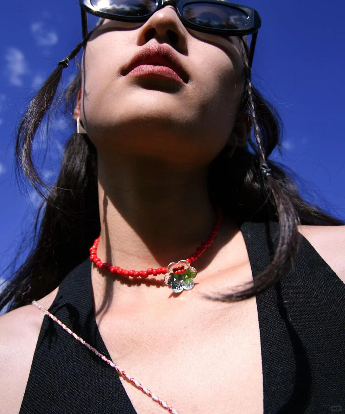 A woman models a Lazesoul handmade beaded necklace featuring a S925 sterling silver flower pendant and vivid red glaze beads, set against a blue sky for a natural, elegant backdrop.