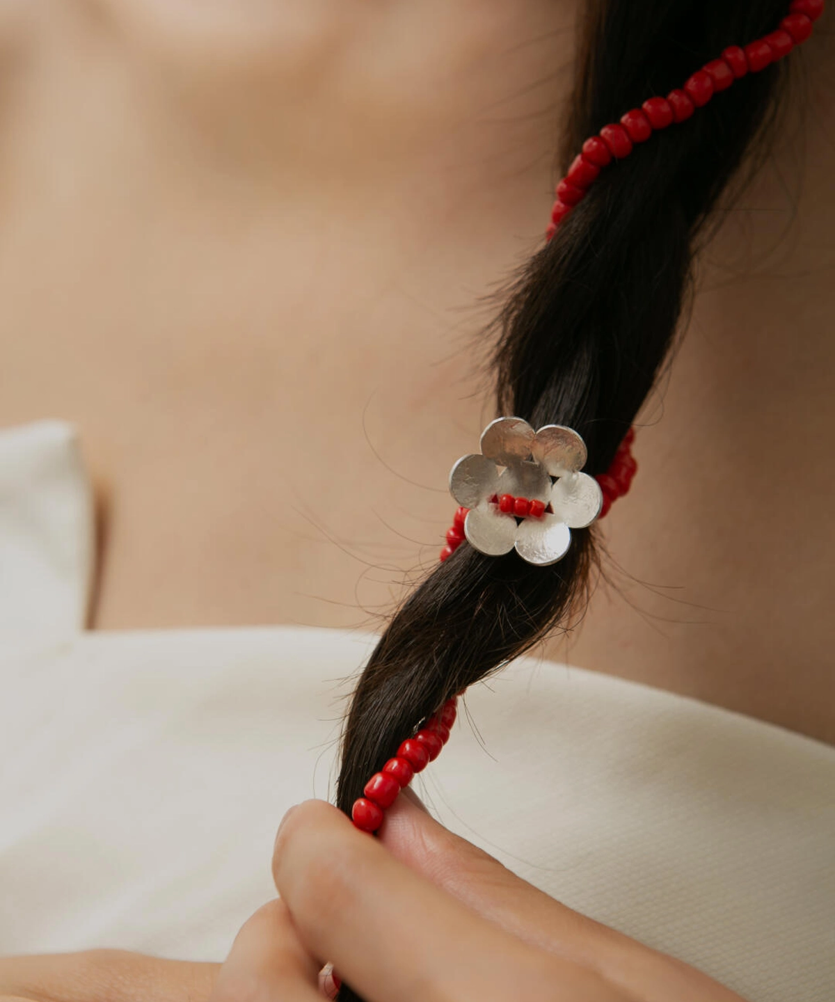 Close-up of a braid adorned with Lazesoul’s Little Flower Beaded Necklace in S925 Sterling Silver. Features red glaze beads and a silver flower charm, showcasing elegant craftsmanship and natural styling.