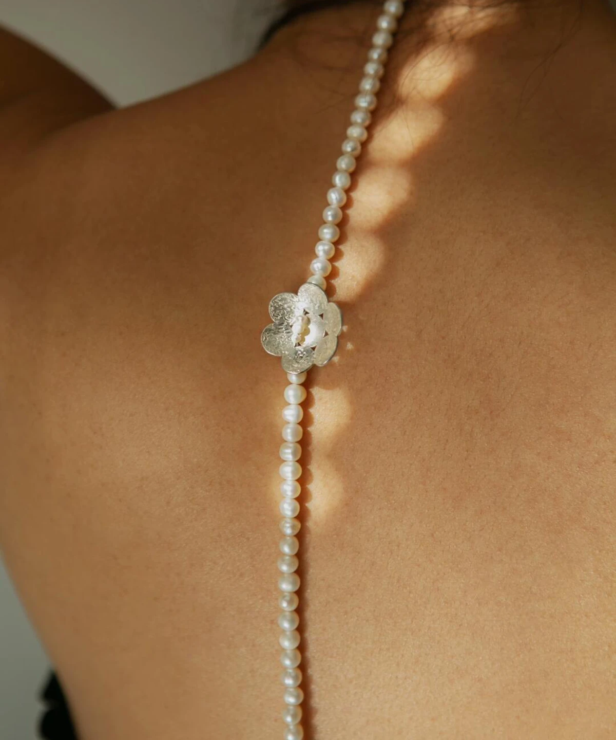 Back view of a woman wearing Lazesoul’s S925 Sterling Silver Little Flower Beaded Necklace with natural freshwater pearls. Delicate silver flower pendant accents the handcrafted design, ideal for elegant, nature-inspired styling.