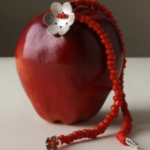 Handmade beaded necklace featuring red glaze beads and a delicate flower charm in S925 sterling silver, elegantly draped over a red apple. Lazesoul natural jewelry with artisan detail and timeless design.