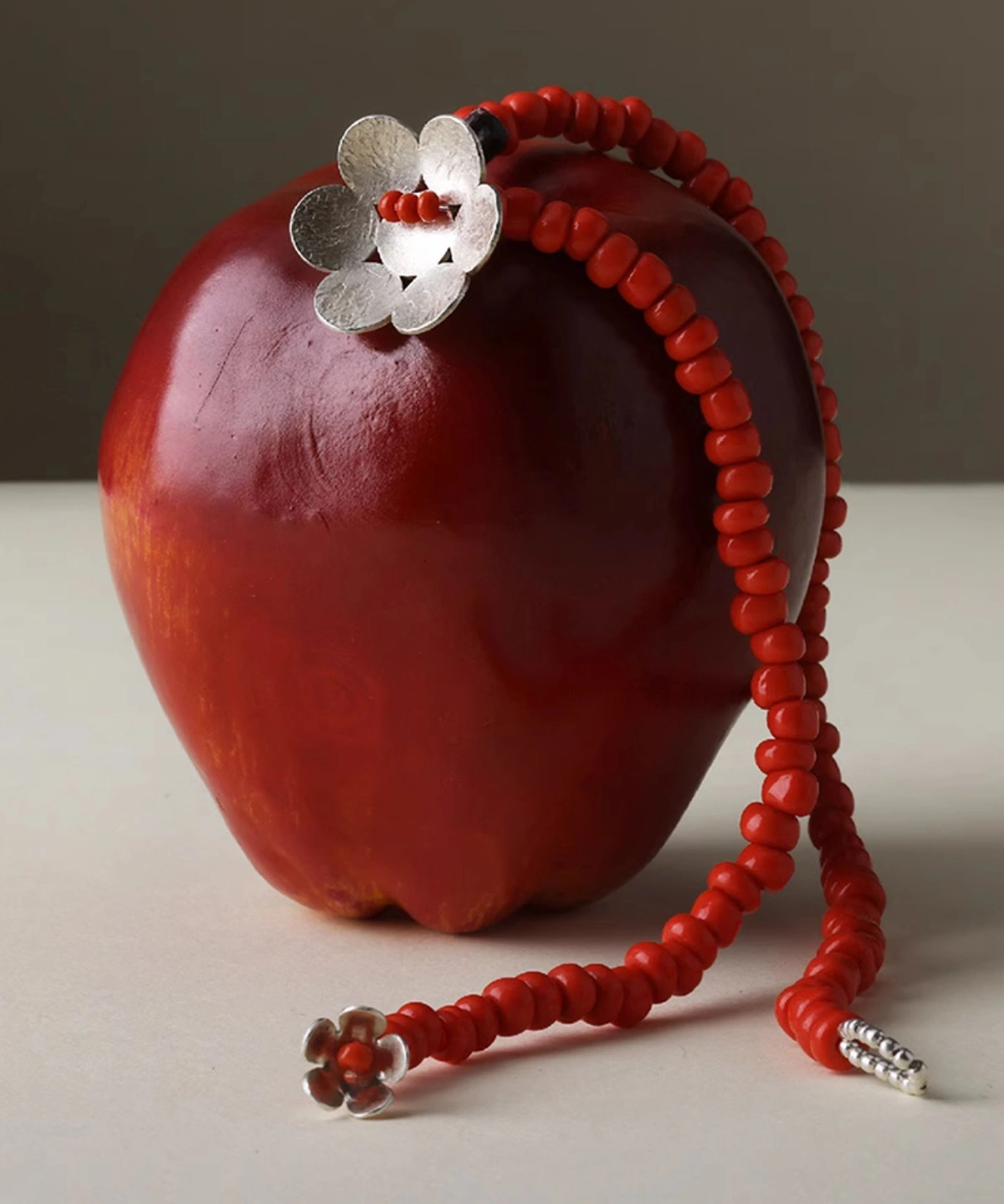 Handmade beaded necklace featuring red glaze beads and a delicate flower charm in S925 sterling silver, elegantly draped over a red apple. Lazesoul natural jewelry with artisan detail and timeless design.