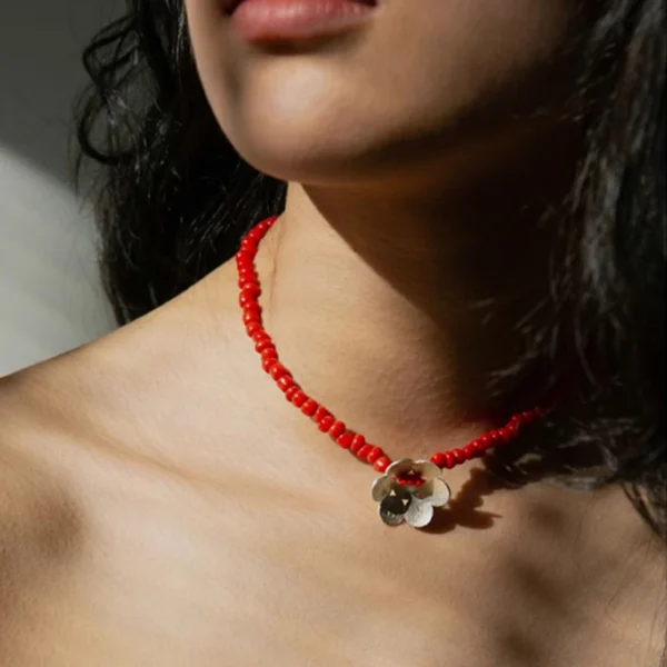 A handmade beaded necklace with a red glaze bead and a delicate sterling silver flower pendant, elegantly worn on the neck, showcasing Lazesoul’s artisanal craftsmanship in S925 sterling silver jewelry.