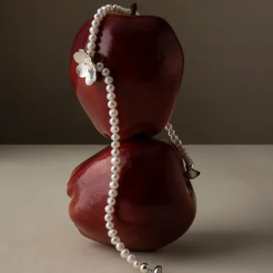 Little Flower Beaded Necklace in S925 Sterling Silver featuring natural freshwater pearls and a delicate silver flower charm, styled over two red apples for a nature-inspired and artisanal jewelry presentation.