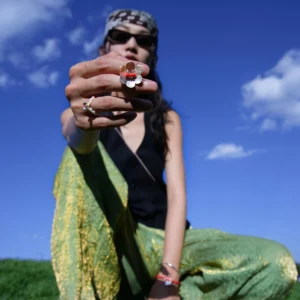 Hand wearing Lazesoul’s Little Flower Beaded Ring in S925 Sterling Silver, featuring a red glaze bead centered in a delicate floral design. Styled outdoors with green pants and a black top.