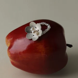 A handmade S925 sterling silver beaded ring featuring a dainty flower design and natural freshwater pearls, artistically placed on a red apple to highlight Lazesoul's signature craftsmanship and organic charm.