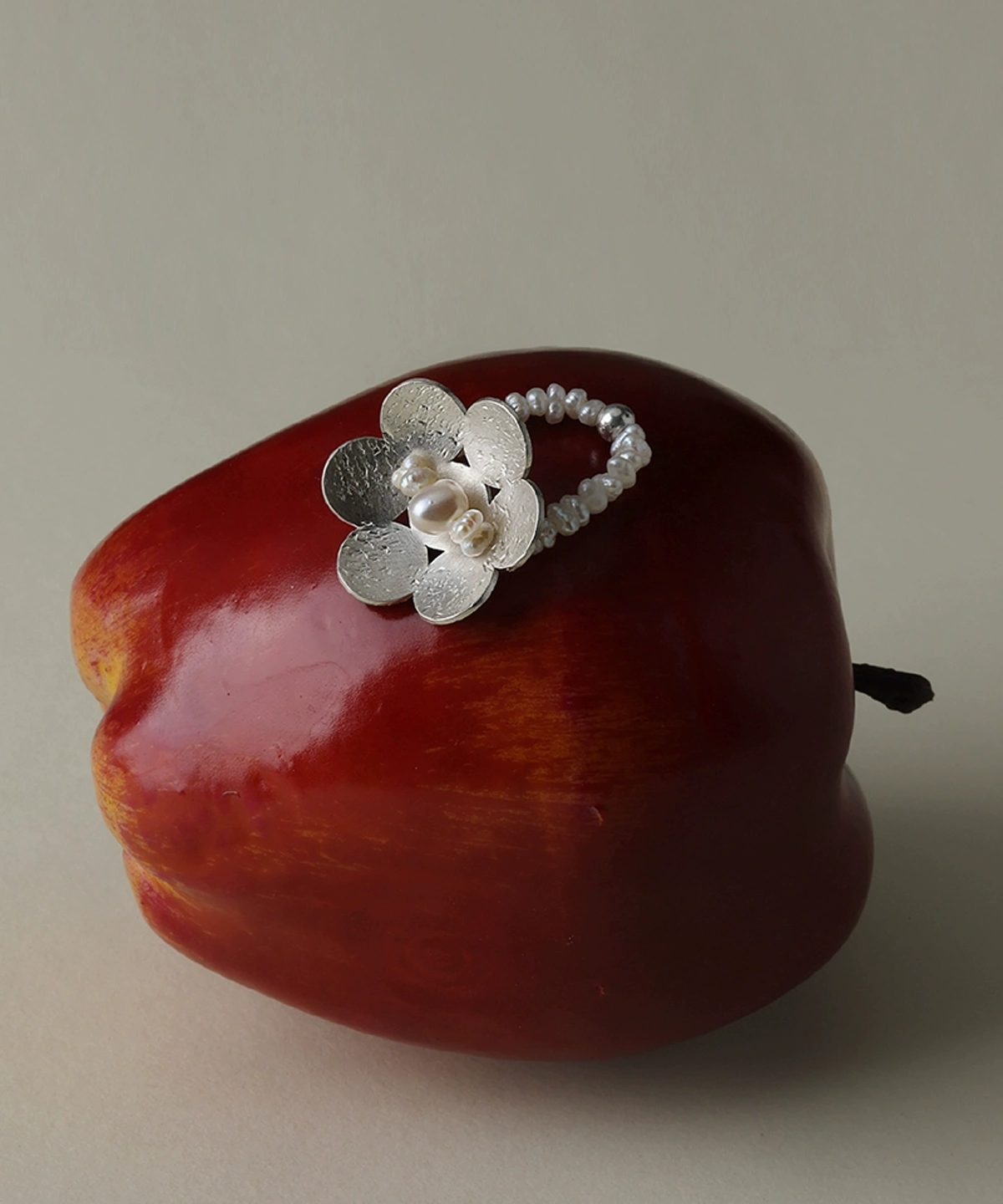 A handmade S925 sterling silver beaded ring featuring a dainty flower design and natural freshwater pearls, artistically placed on a red apple to highlight Lazesoul's signature craftsmanship and organic charm.
