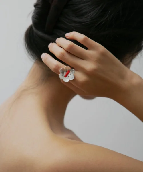 A handmade little flower beaded ring in S925 sterling silver with a red glaze bead, worn on the left hand. The elegant natural jewelry piece is from Lazesoul and crafted with delicate artisanal detail.
