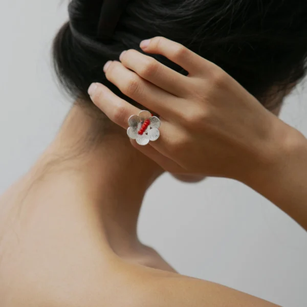 A handmade little flower beaded ring in S925 sterling silver with a red glaze bead, worn on the left hand. The elegant natural jewelry piece is from Lazesoul and crafted with delicate artisanal detail.