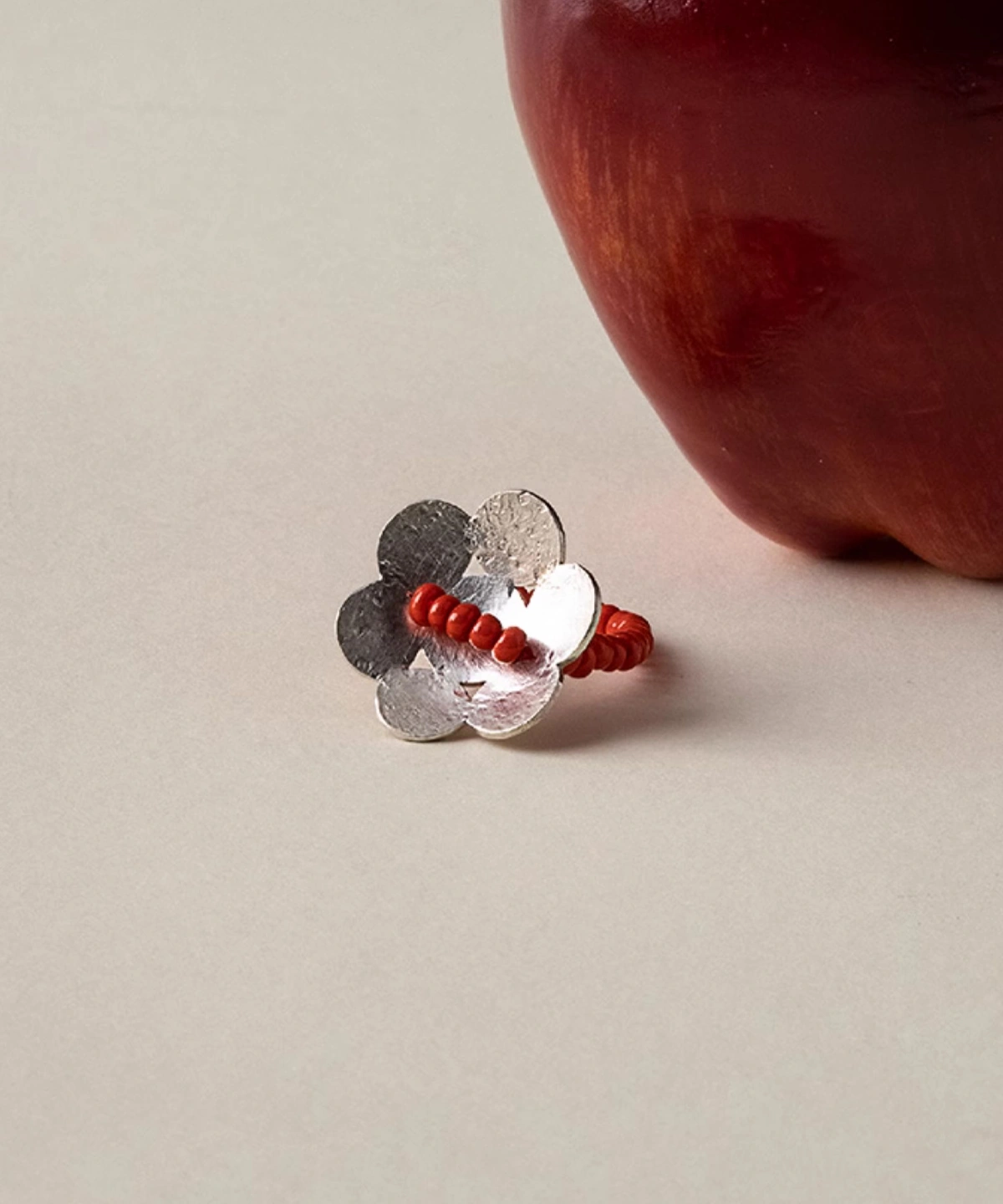 Handmade beaded ring in S925 sterling silver with a red glaze flower design, positioned beside a red apple to highlight its natural elegance and artisan craftsmanship.