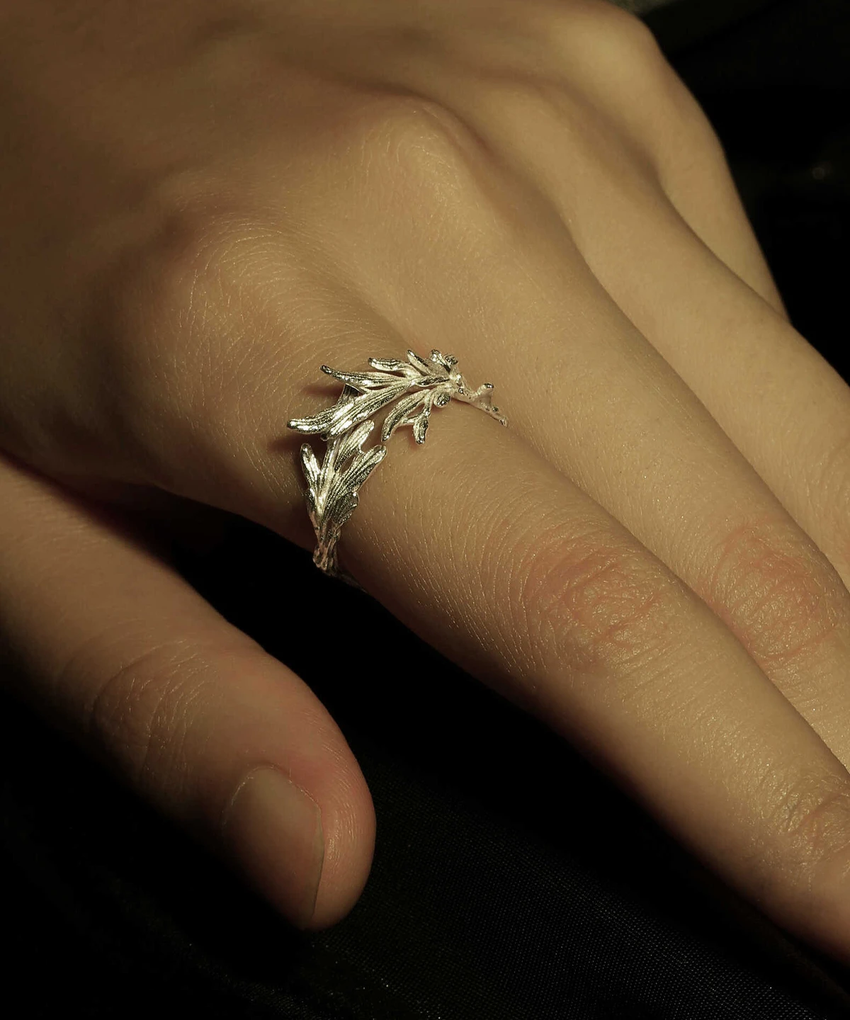 Close-up of a hand wearing the New Leaf Adjustable Sterling Silver Leaf Ring from Lazesoul Handmade Natural Jewelry. The silver ring features a nature-inspired branch design with high shine against a dark background, emphasizing elegance.