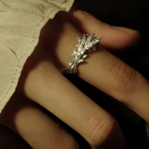 Close-up of a hand wearing a Sterling Silver Leaf Ring with a detailed branch-inspired design; the ring rests on a light fabric sleeve, capturing its intricate textures and organic craftsmanship.