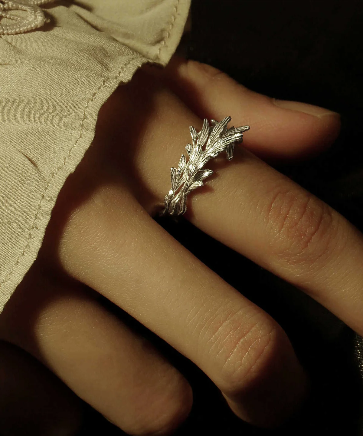 Close-up of a hand wearing a Sterling Silver Leaf Ring with a detailed branch-inspired design; the ring rests on a light fabric sleeve, capturing its intricate textures and organic craftsmanship.