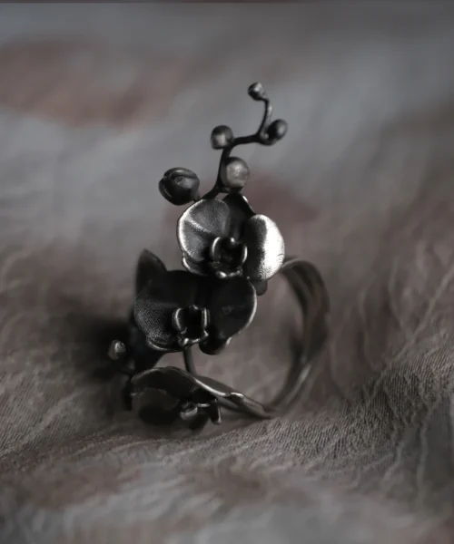 Lazesoul’s handmade Orchid Ring in oxidized S925 sterling silver, showcasing sculpted orchid flowers and buds with a vintage patina. The adjustable design enhances comfort and elegance, set on textured fabric to highlight artisanal detail.