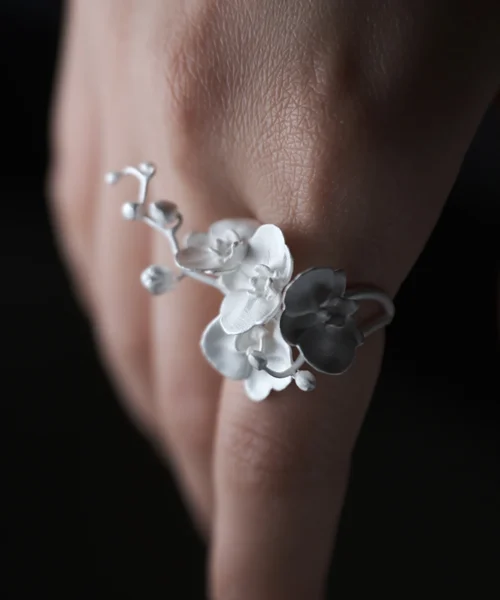 Close-up of a Lazesoul Orchid Ring crafted in S925 sterling silver, featuring delicate orchid petals and an adjustable band; nature-inspired handmade jewelry styled on a woman's hand. Orchid Ring design highlights floral elegance and artisanal detail.