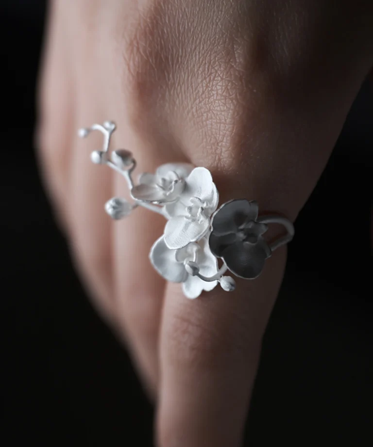 Close-up of a Lazesoul Orchid Ring crafted in S925 sterling silver, featuring delicate orchid petals and an adjustable band; nature-inspired handmade jewelry styled on a woman's hand. Orchid Ring design highlights floral elegance and artisanal detail.