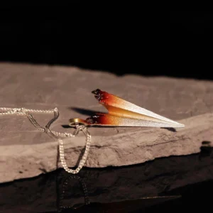 A close-up image of a handmade S925 sterling silver paper airplane necklace. The necklace features a delicate chain and a pendant shaped like a paper airplane, with a gradient color effect transitioning from silver to a warm brown hue.