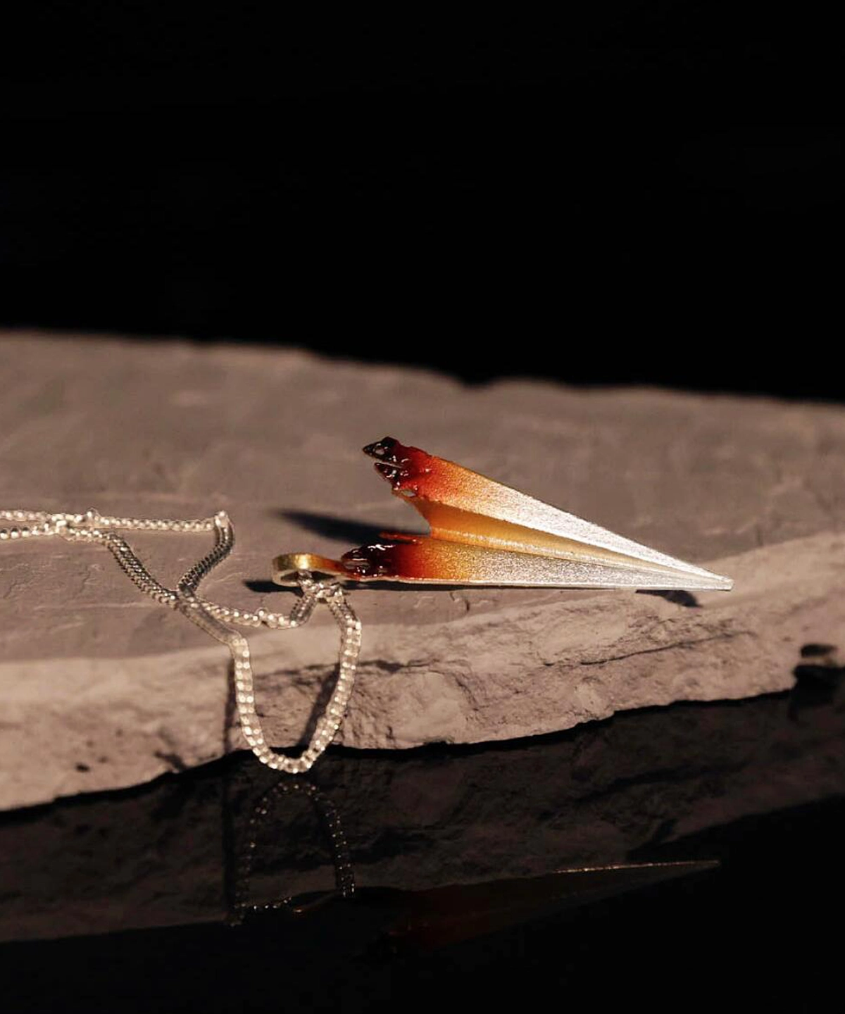 A close-up image of a handmade S925 sterling silver paper airplane necklace. The necklace features a delicate chain and a pendant shaped like a paper airplane, with a gradient color effect transitioning from silver to a warm brown hue.