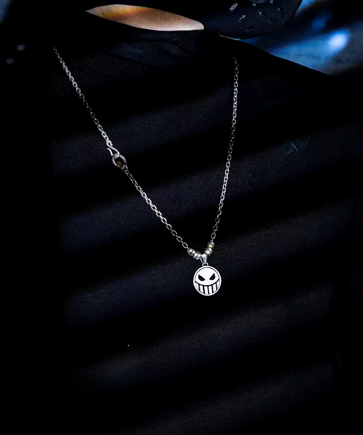 A close-up view of a S925 Silver Pirate Necklace featuring a reversible Laugh & Cry Face Spinner Pendant, worn against a dark, shadowed background; handmade anime jewelry inspired by One Piece.