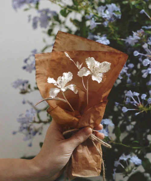 Hand holding a mini Iris Bouquet crafted from 925 sterling silver, wrapped in rustic brown paper with twine. A Lazesoul Handmade Art Gift, this silver floral arrangement blends artistry and elegance, perfect for timeless keepsakes.