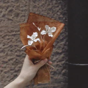 Hand holding a mini 925 sterling silver Iris Bouquet wrapped in rustic brown paper. Handmade Art Gifts by Lazesoul, blending delicate craftsmanship with timeless elegance for unique Iris Bouquet jewelry and keepsakes.